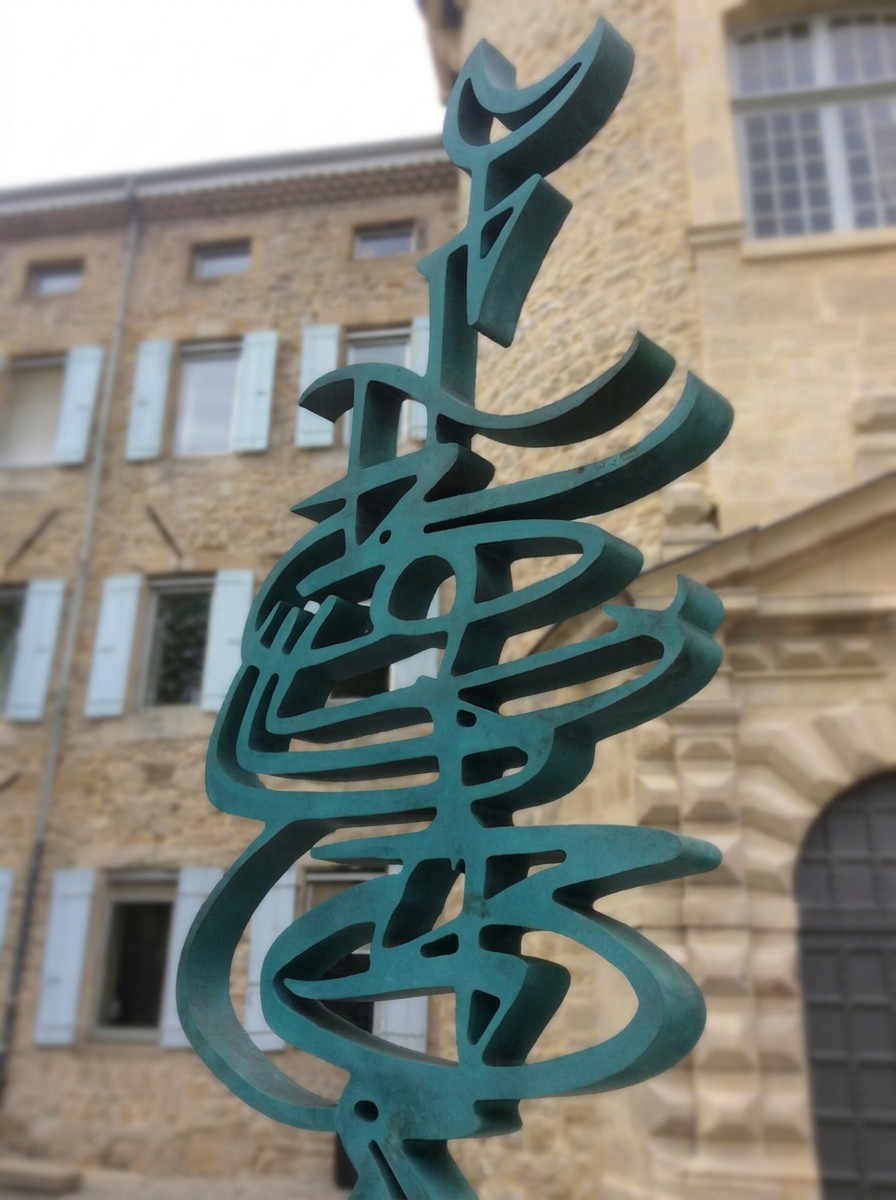 Sculpture patinée verte devant une façade en pierre